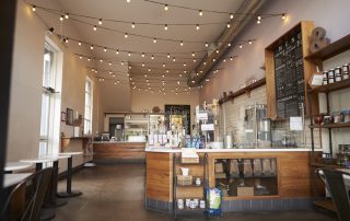 Warm beige painted cafe interior with string lighting, wood counter, chalkboard menu, and tall windows. commercial interior painting cost Atlanta