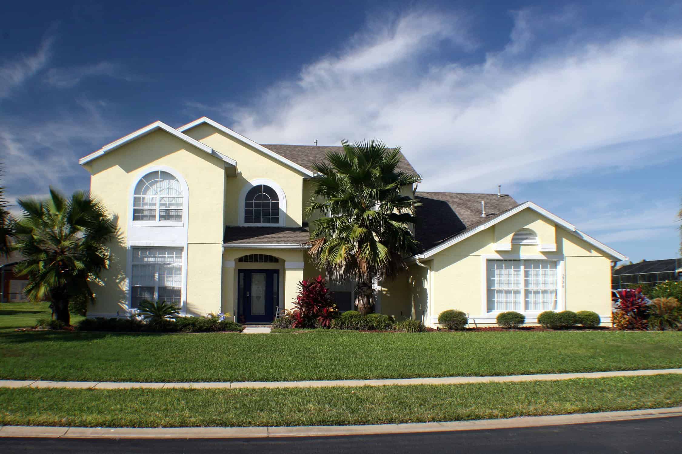 Cream Painted Two-Story Home Cream-painted two-story residential home with dark roof, arched windows, and palm tree landscaping.