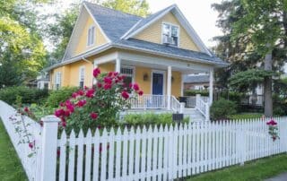 Yellow exterior residential home with white trim, dark roof, and white picket fence in Atlanta, GA exterior house painting cost