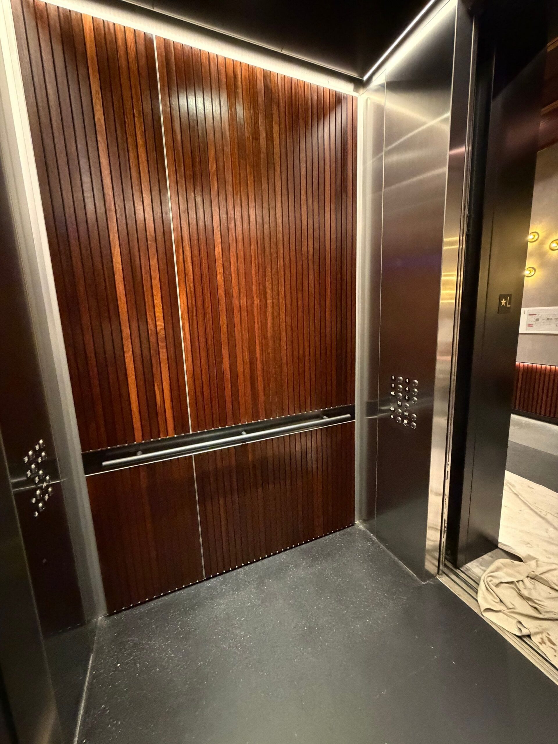 Commercial Elevator Wood Panel Finishing Services Luxurious commercial elevator interior featuring polished dark wood paneling and sleek stainless steel accents.
