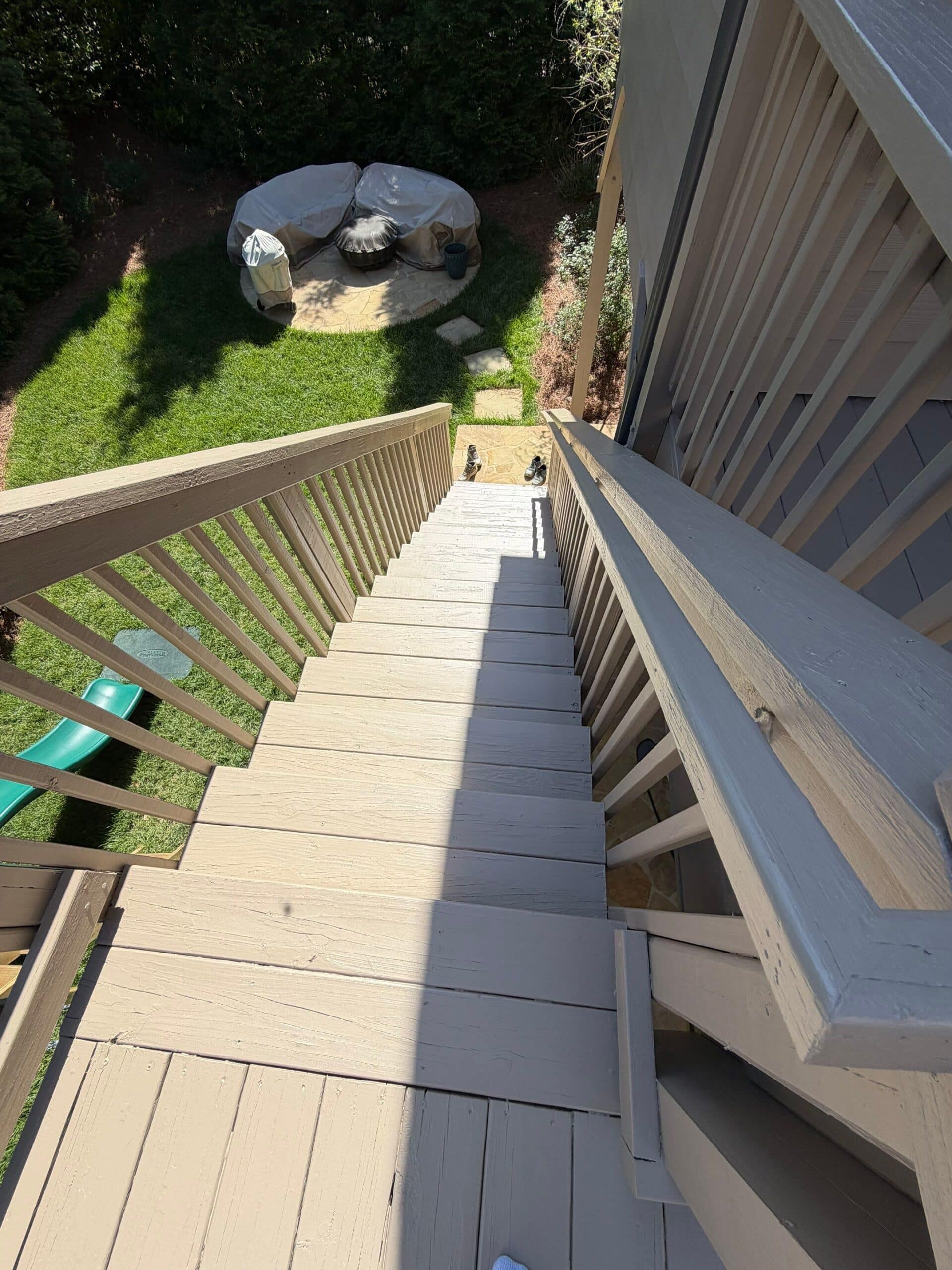 Professional Deck and Stair Painting Services A freshly painted light beige wooden deck staircase leading down to a green backyard with a fire pit.