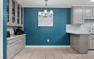 Teal painted residential kitchen feature wall with white cabinetry, herringbone tile backsplash, and pendant lighting.