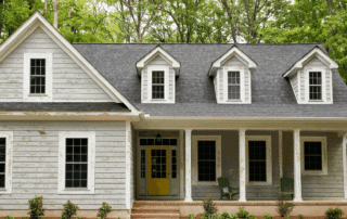 White horizontal siding farmhouse with gray roof, white dormers, yellow entry door, and front porch columns in Atlanta, GA.