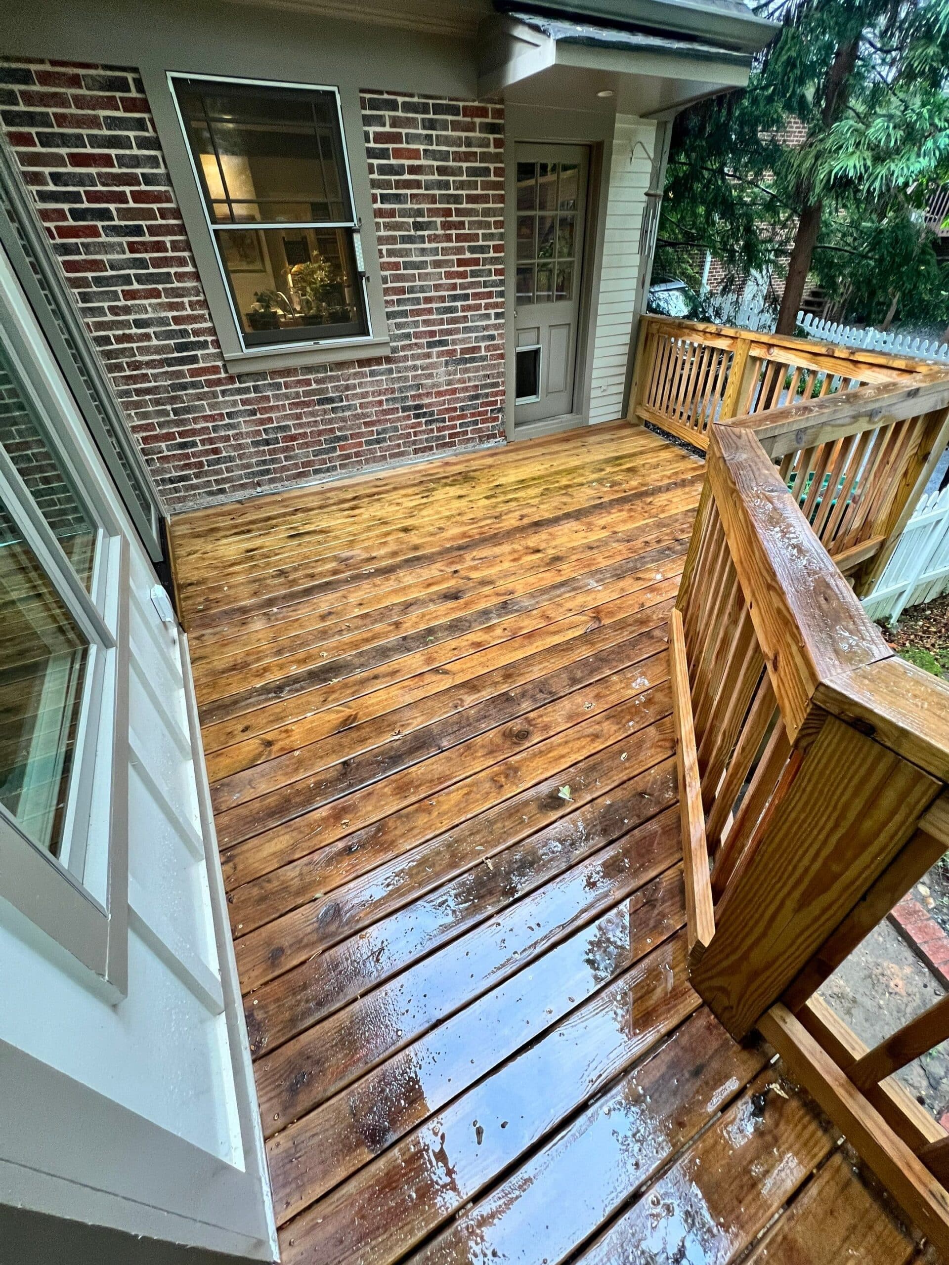 Wood Deck Stain Before Restoration Weathered golden-brown stained wood deck with peeling finish, white-trimmed brick home, and wooden railings.