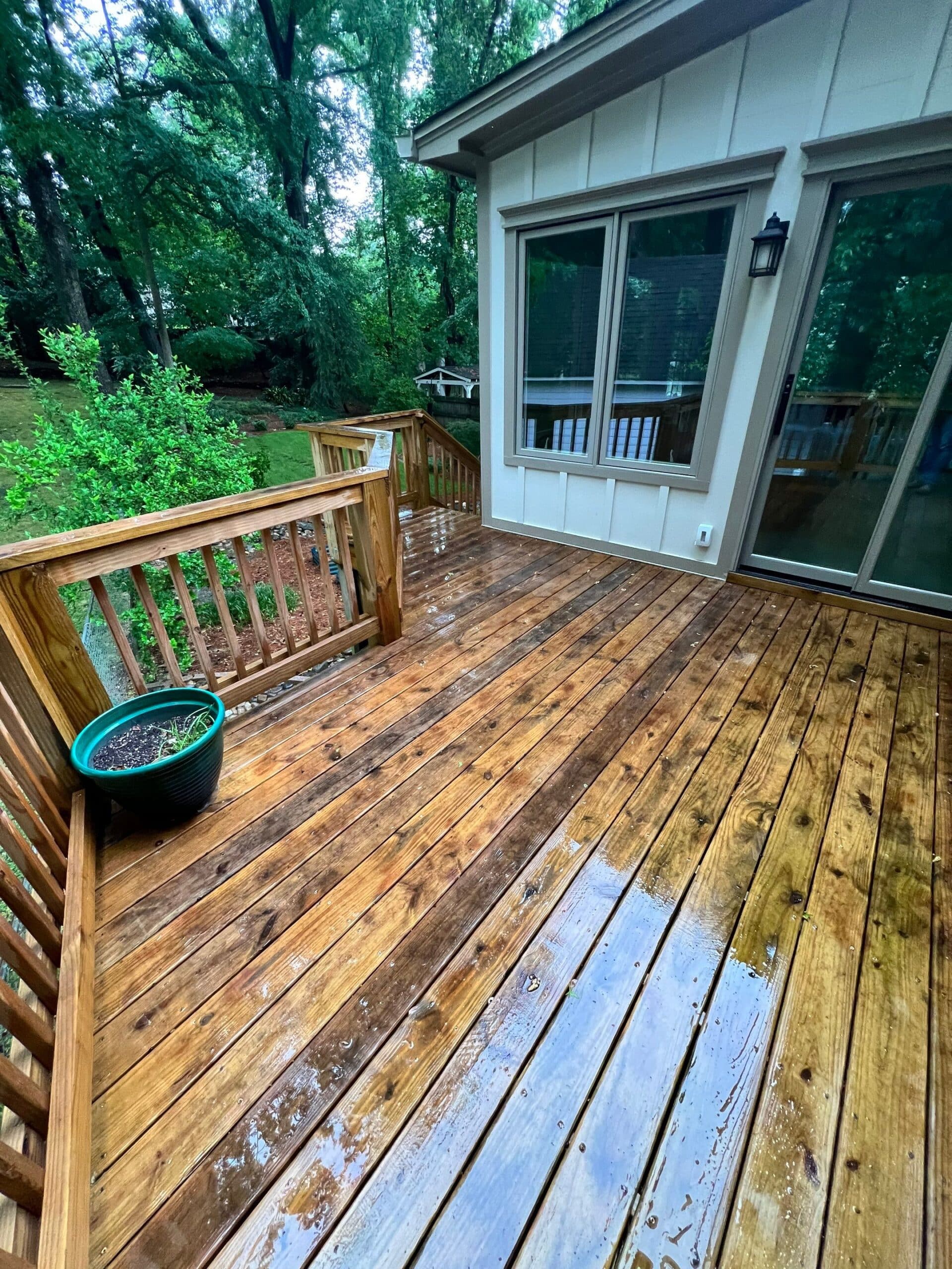 Wood Deck Before Refinishing Medium-brown stained wood residential deck with peeling finish, vertical railings, and white-trimmed glass doors on home
