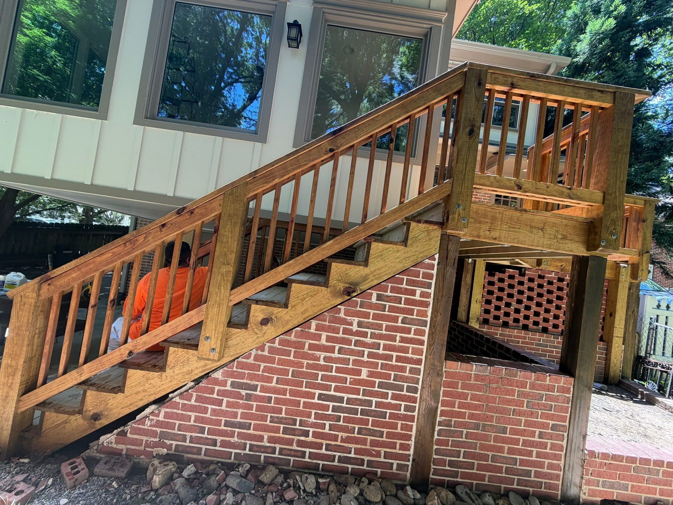 Wood Deck Stairs With Railings Medium-brown stained wood deck stairs with vertical railings and mixed finish boards descending to brick patio.
